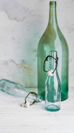 A large and a small vintage green glass bottle sit on a light, textured surface, casting soft shadows.の写真素材