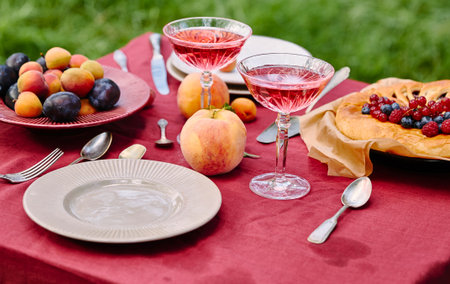 A delightful outdoor picnic spread featuring a variety of fresh fruits, two glasses of pink beverage, and a rustic fruit tart.の写真素材