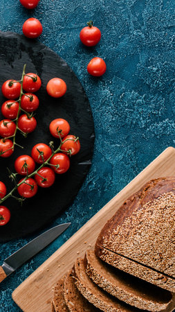 A rustic arrangement of vibrant cherry tomatoes on a dark plate alongside sliced whole wheat bread...