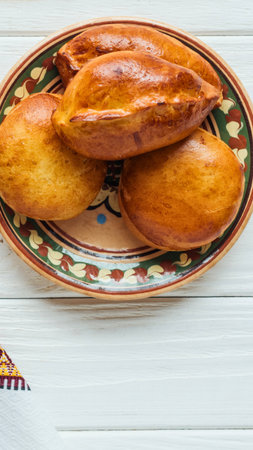 A close-up view of three golden-brown baked pastries arranged on a colorful, ornate plate, presented on a white wooden surface.の写真素材