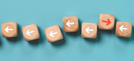 Several wooden blocks are laid out on a teal background. Most have white arrows pointing left, but one has a red arrow pointing right.の写真素材