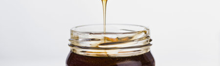 A thin stream of viscous golden honey is being poured into a clear glass jar with a textured rim.の写真素材