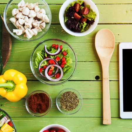 A vibrant overhead view of fresh ingredients, spices, and cooking tools arranged on a green wooden surface, ready for a healthy meal.の写真素材