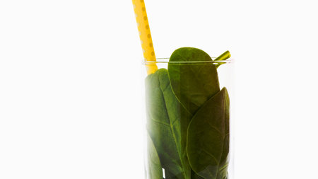 A tall glass filled with vibrant green juice, featuring a bright yellow straw, presented against a clean white background.の写真素材