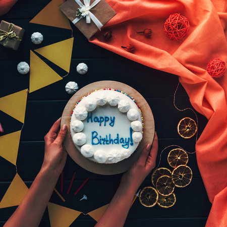 Overhead view of hands presenting a white frosted cake with blue lettering and surrounding party decorations.の写真素材