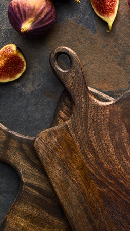 A close-up overhead shot of a dark, textured wooden cutting board with ripe figs, some whole and some sliced, scattered around.の写真素材