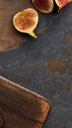 Close-up of sliced ripe figs artfully arranged on a textured, dark, rustic surface with a piece of wood.の写真素材