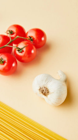 A simple still life featuring spaghetti, cherry tomatoes on the vine, and a head of garlic on a light background.の写真素材