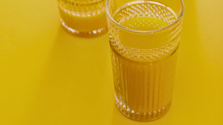 Two tall glasses filled with vibrant orange juice sit on a bright yellow surface, suggesting a refreshing and sunny beverage.の写真素材