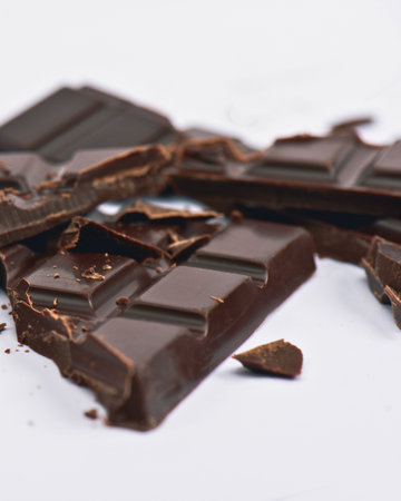 Several pieces of dark chocolate, some broken and scattered, lie on a clean white surface, creating an appealing food still life.の写真素材