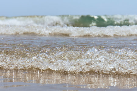 Close-up view of foamy ocean waves rolling onto a wet sandy beach under a clear sky.の写真素材