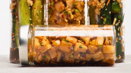 A collection of various preserved foods, including pickles and chutneys, neatly arranged in transparent glass jars on a light surface.の写真素材