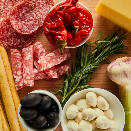 A top-down view of a rustic charcuterie board featuring cured meats, cheese, olives, breadsticks, garlic, and herbs.の写真素材