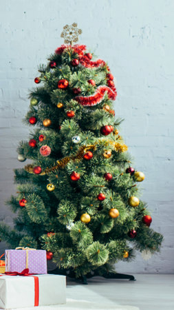 A fully decorated Christmas tree adorned with ornaments and garland sits beside wrapped gifts, ready for the holidays.の写真素材