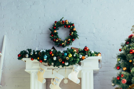 A white mantelpiece adorned with garland and ornaments, topped by a Christmas wreath. A decorated tree stands to the right.の写真素材