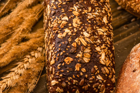 A detailed view of a rustic granola bar packed with various seeds and grains, set against a backdrop of wheat stalks.の写真素材