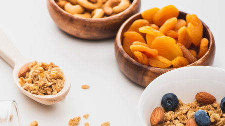 A top-down view of wooden bowls filled with granola, cashews, and dried apricots, with a spoon of granola in the foreground.の写真素材