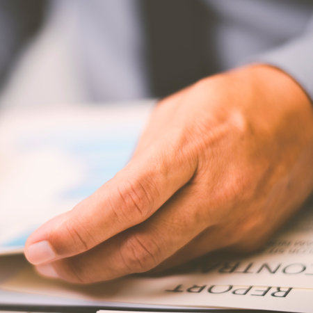 A man's hand is gently placed on a document with visible text, suggesting reading or reviewing.の写真素材