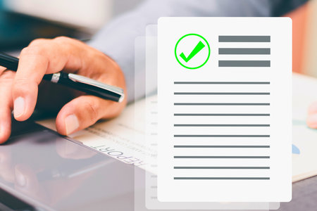 A hand holds a stamp, pressing it onto a document that features a green checkmark indicating approval or completion.の写真素材