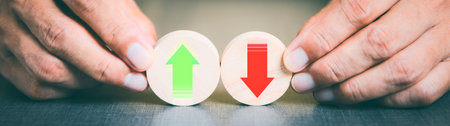 Two oval tokens with a green upward arrow and a red downward arrow are held by hands, symbolizing financial or market trends.の写真素材