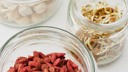Close-up of dried goji berries, sprouts, and other ingredients stored in clear glass jars on a white surface.の写真素材