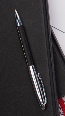 A close-up shot features a modern black pen with a shiny silver clip and tip, positioned diagonally on a textured dark background.の写真素材