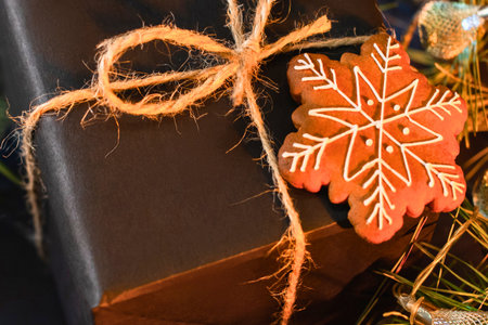 A close-up of a dark gift box tied with rustic twine, adorned with a snowflake-shaped gingerbread cookie and greenery.の写真素材