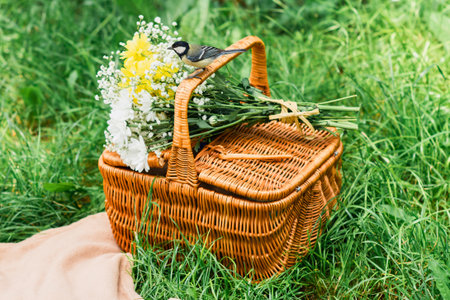 A woven wicker picnic basket is filled with a vibrant bouquet of wildflowers, set against a backdrop of lush green grass.の写真素材