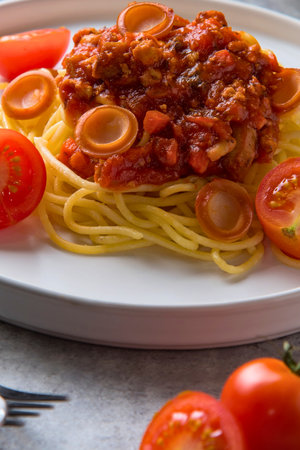 A close-up shot of a plate of spaghetti topped with rich meat sauce and garnished with sliced fresh tomatoes.の写真素材