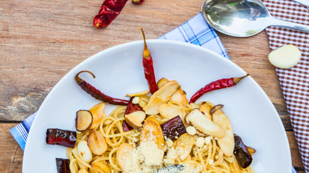 A close-up overhead view of a plate of spicy noodles garnished with dried chilies and garlic, set on a rustic wooden surface.の写真素材