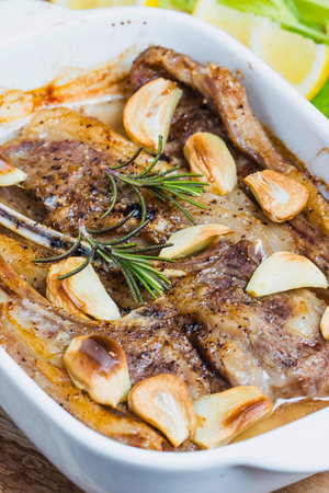 A close-up of tender, roasted pork slices seasoned with fresh garlic and rosemary, baked in a white ceramic dish.の写真素材