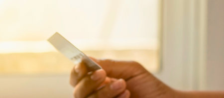 A human hand holds a sharp, translucent shard of glass against a softly blurred, warm-toned background.の写真素材