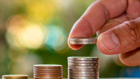 A close-up shot shows a person's hand carefully placing a coin on top of a growing stack, symbolizing financial accumulation and investment.の写真素材