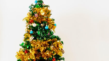 A vibrant, artificial Christmas tree adorned with colorful ornaments, gold and green tinsel, and lights against a plain background.の写真素材