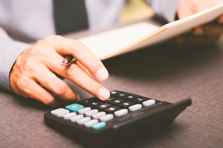 A person's hands are shown using a calculator and holding a document, suggesting financial work or calculations.の写真素材