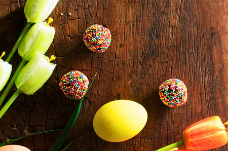 A top-down view of colorful, decorated Easter eggs and vibrant tulips arranged on a rustic wooden background, evoking a festive spring atmosphere.の写真素材