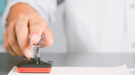 A close-up shot of a hand holding a rubber stamp and pressing it down onto a document, signifying approval or official action.の写真素材