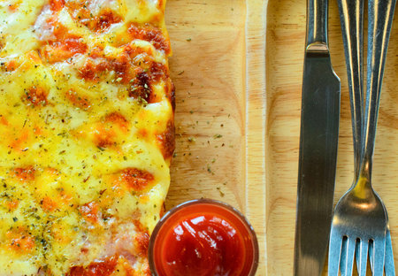 A delicious, cheesy pizza slice is presented with a small dish of ketchup and a fork and knife, ready to be enjoyed.の写真素材