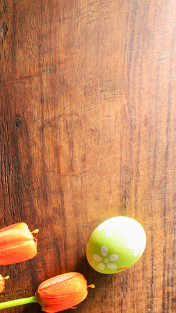 A close-up shot of vibrant orange flowers and a green egg resting on a textured wooden background.の写真素材