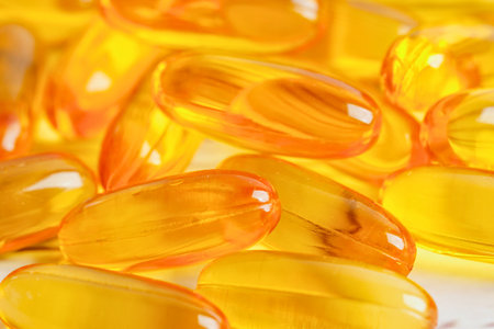 A macro shot of many oval shaped, translucent golden capsules, possibly supplements, piled together.の写真素材