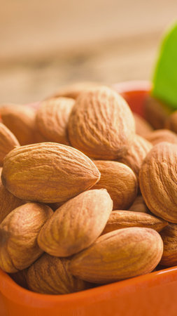 A close-up shot of a pile of whole, raw almonds in an orange bowl, with a hint of green in the background.の写真素材