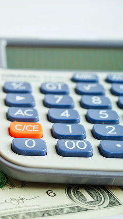 A detailed view of a calculator's buttons, including an orange key, resting on a bed of US dollar bills.の写真素材