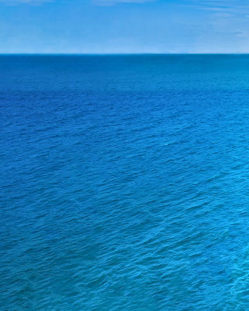 A serene, expansive view of the deep blue ocean meeting a bright, cloudless sky at the horizon.の写真素材