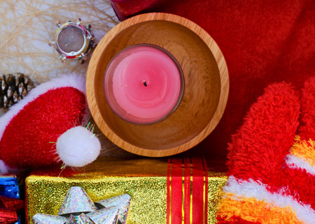 A festive arrangement featuring a pink candle in a wooden bowl, surrounded by Christmas gifts and red decorations.の写真素材