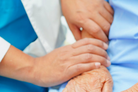 A close-up shows a caregiver's hands holding a patient's arm, conveying empathy and support in a healthcare environment.の写真素材