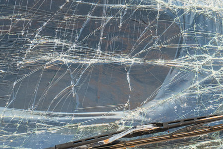 A detailed view of a damaged car windshield, showcasing a complex network of spiderweb cracks and a wiper blade.の写真素材