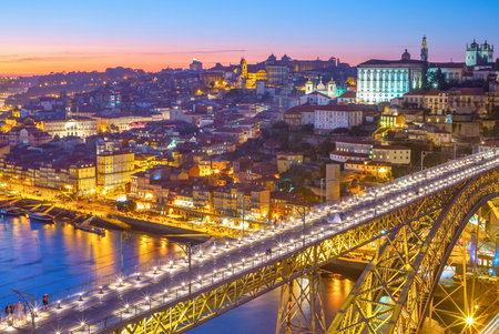 A vibrant cityscape of Porto, Portugal, featuring the Dom LuÃ­s I Bridge, the Douro River, and illuminated buildings at twilight.の写真素材