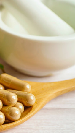 Close-up of light brown herbal capsules arranged on a wooden spoon, with a blurred white bowl in the background.の写真素材