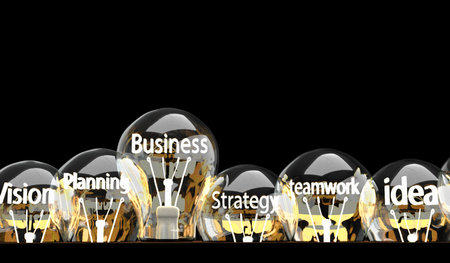 A row of illuminated lightbulbs, each containing business-related words like 'Vision', 'Planning', 'Strategy', 'Teamwork', and 'Idea', against a dark background.の写真素材