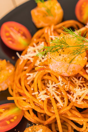 A close-up shot of a plate of spaghetti with a rich tomato sauce, topped with shrimp and sprinkled with cheese and herbs.の写真素材